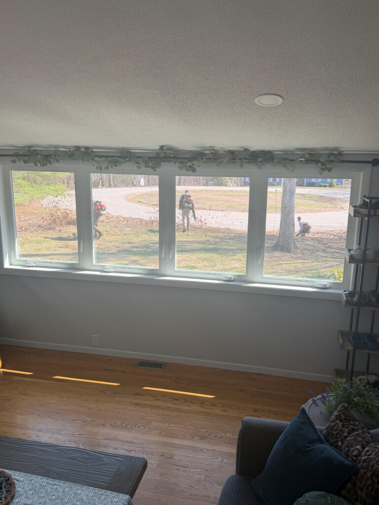 Spring cleanup season is underway in Windham, NH, and this view from inside the home says it all. As the homeowner relaxes indoors, the crew from Sweeet Landscaping is hard at work outside—clearing leaves, freshening up the lawn, and getting the property ready for the growing season.